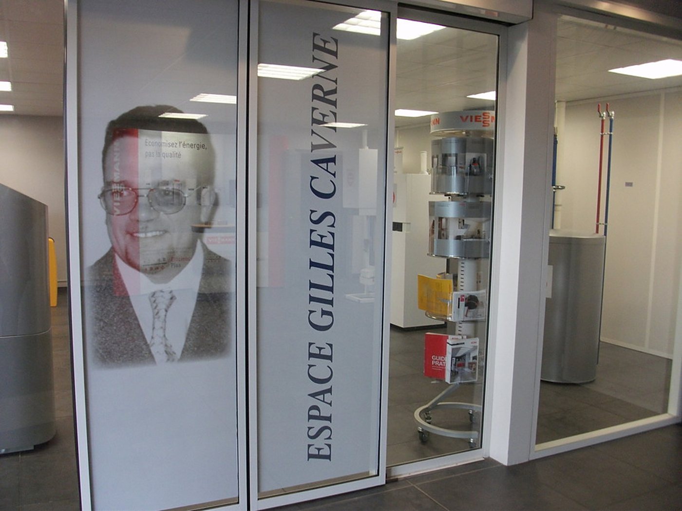 Vitrine vitrée de l'Espace Gilles Caverne avec un portrait d'homme sur la vitre et un présentoir de brochures derrière.