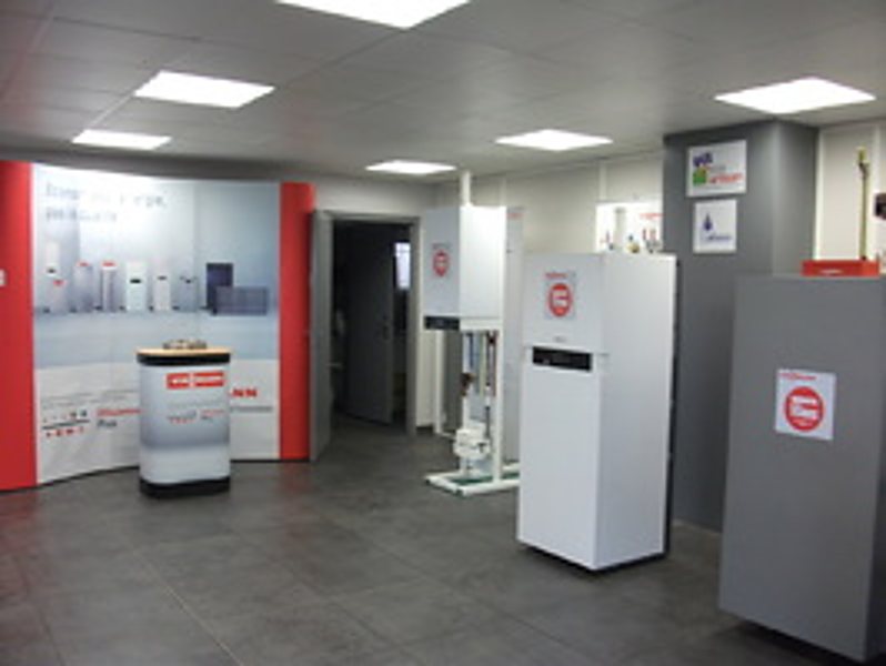 Intérieur d'un showroom présentant plusieurs chaudières et appareils de chauffage blancs devant des panneaux rouges et blancs.